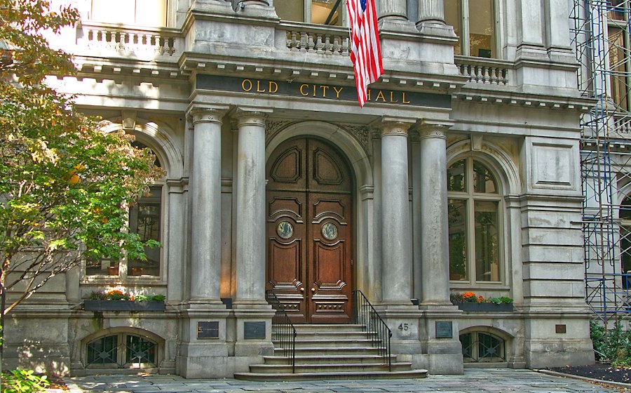 The columned entrance of a city hall, with an American flag above the doors